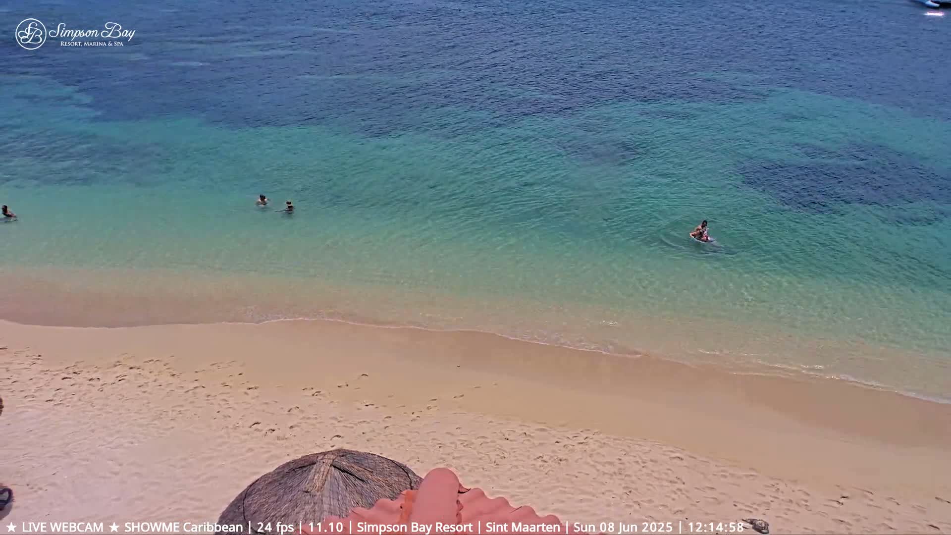 A sandy beach meets clear, shallow turquoise water where several people swim on a sunny day.