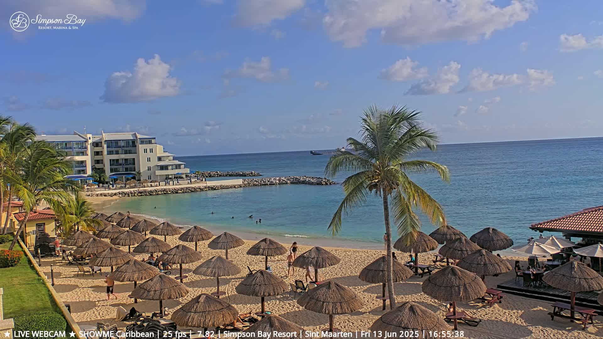 A sandy beach with numerous thatched umbrellas, a calm turquoise ocean, and a resort building under a partly cloudy sky.