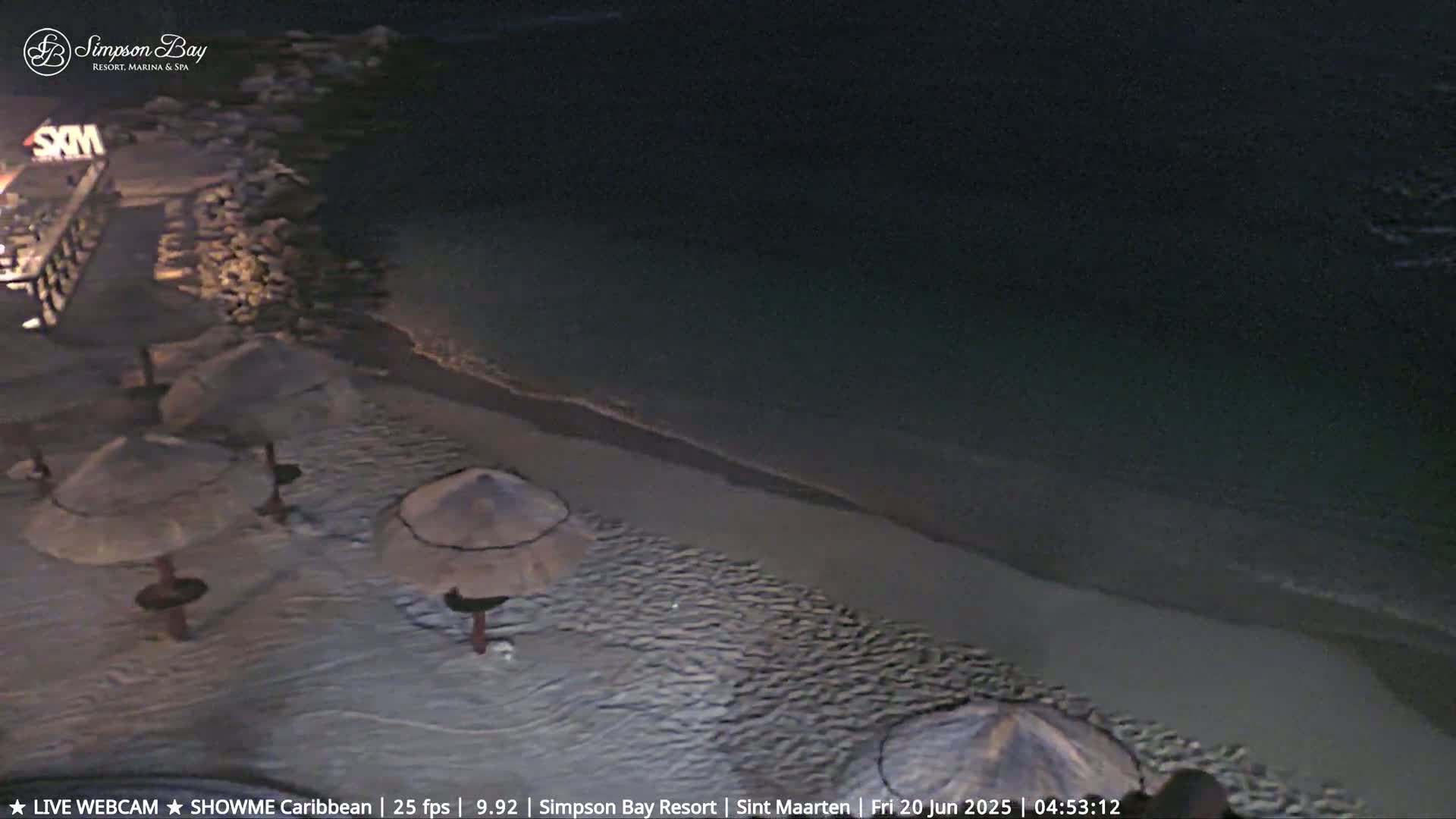 A dark, sandy beach at night with several closed umbrellas and a calm, dark ocean.