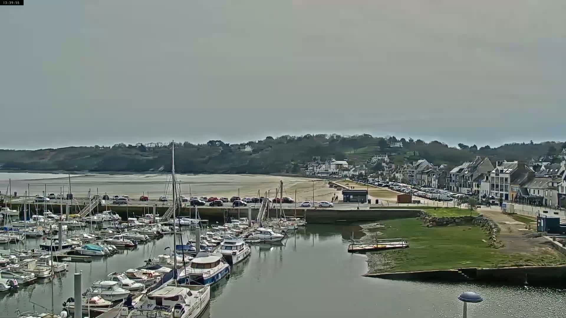 A harbor filled with numerous boats is situated next to a town and beach under an overcast sky.