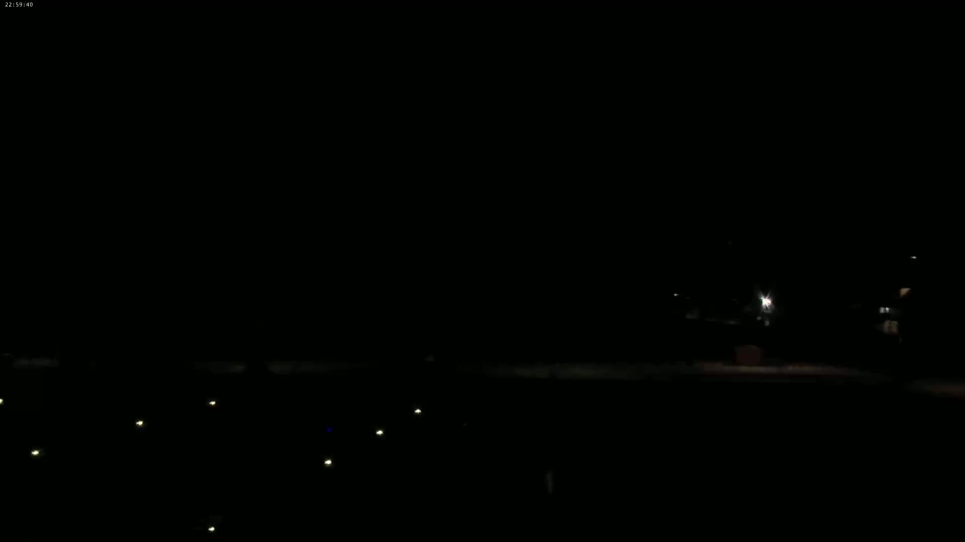 A dark, nighttime scene shows a few faint lights on the ground and a dimly lit area in the distance under a clear, dark sky.
