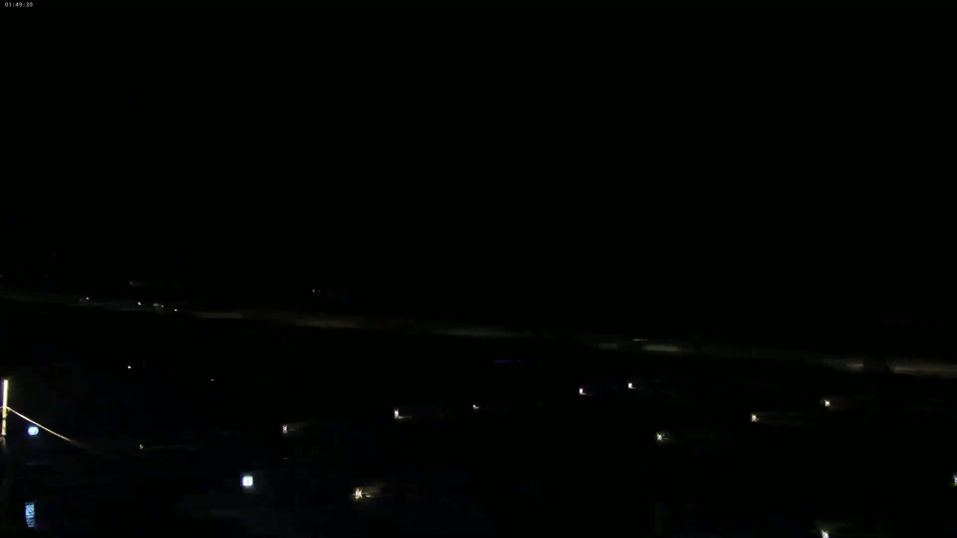 A nighttime, outdoor scene shows a dark expanse of land with a few scattered lights, possibly indicating buildings or vehicles.