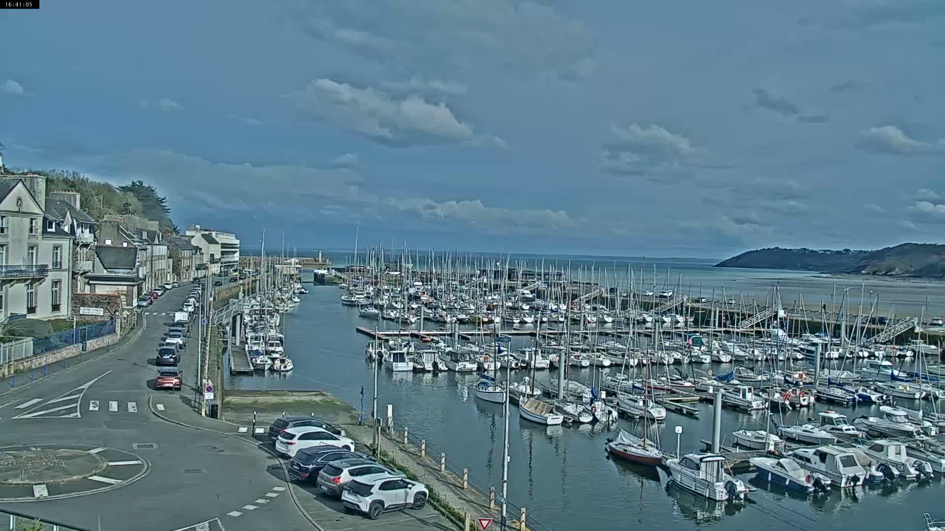 A harbor filled with numerous sailboats and motorboats is seen from a high vantage point on a partly cloudy day.