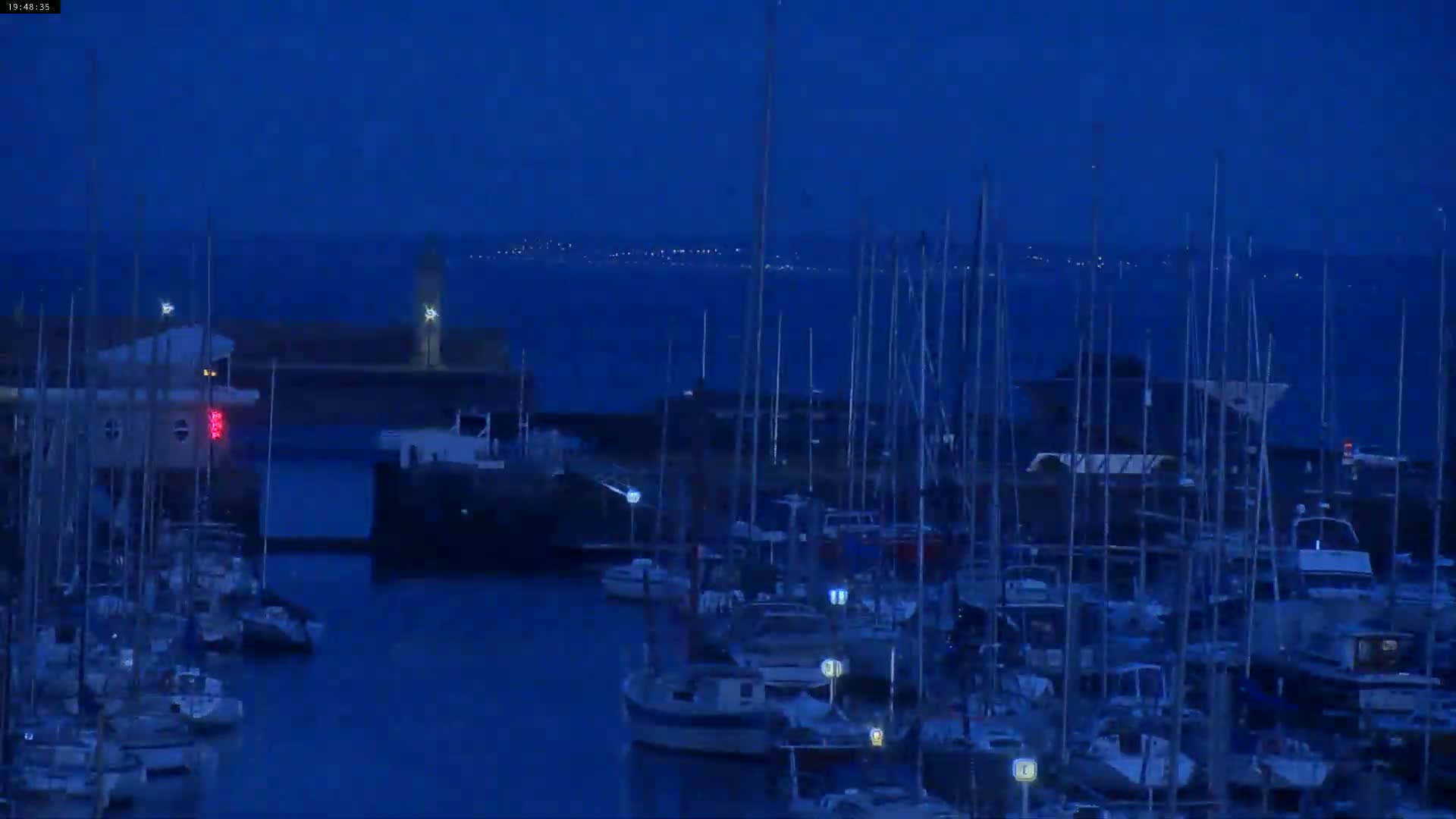 Many sailboats are docked in a harbor at twilight under a dark blue sky.