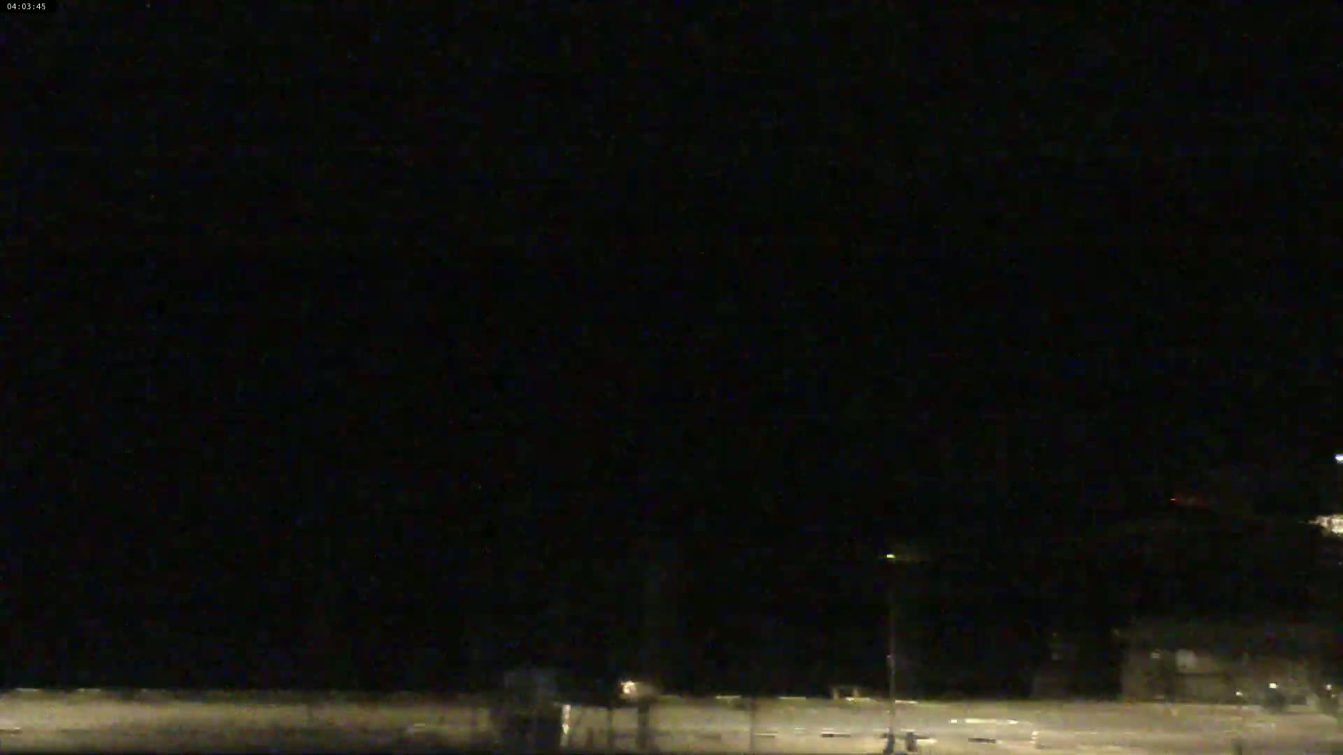 A dark, nighttime scene shows a mostly empty roadway with a few faint lights and indistinct shapes in the distance.
