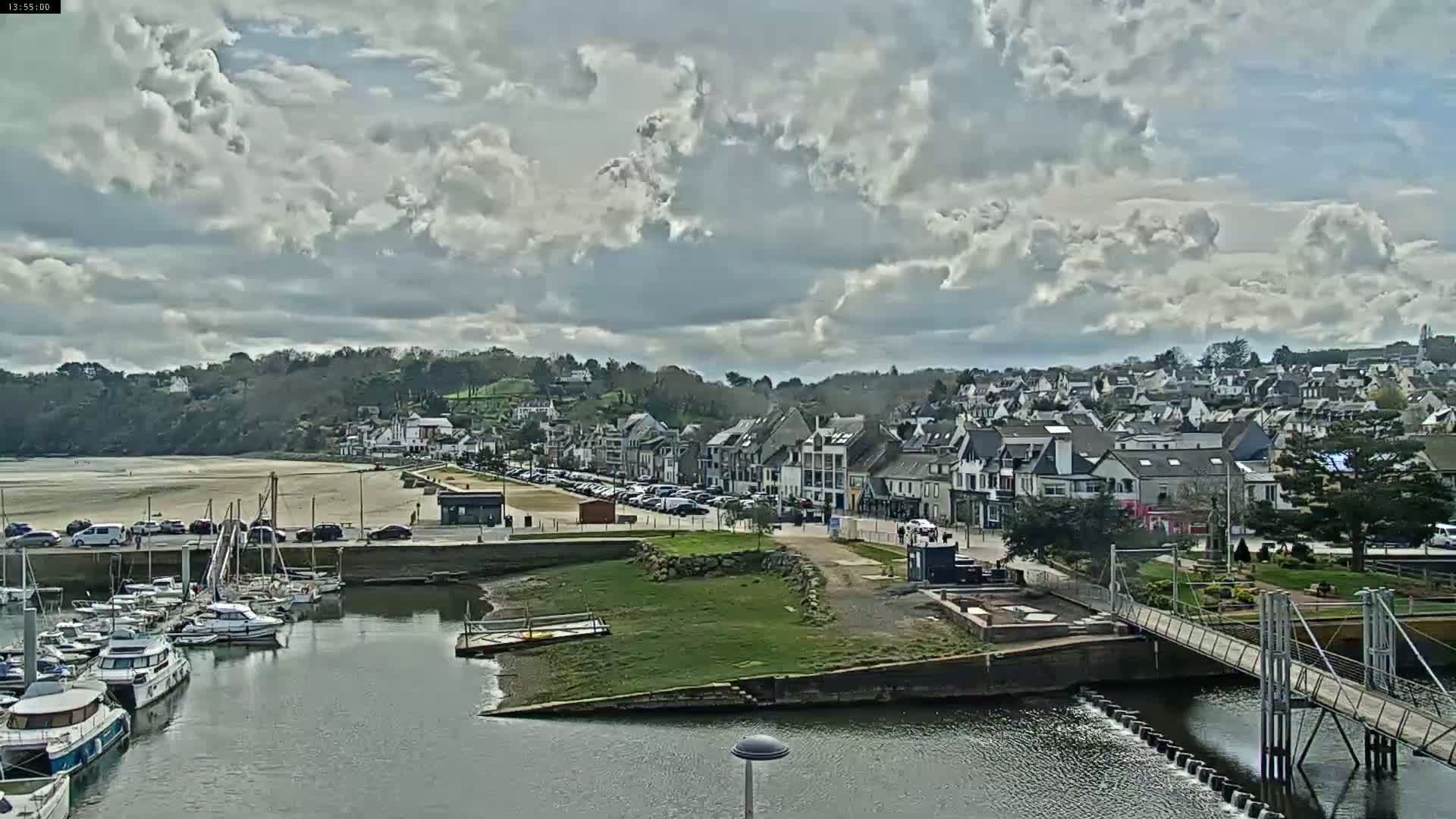 A coastal town with a marina filled with boats sits under a partly cloudy sky.