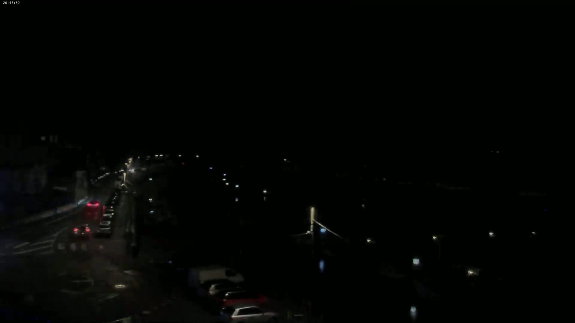 A nighttime, high-angle view shows a dark street with sparsely spaced cars and faint lights.