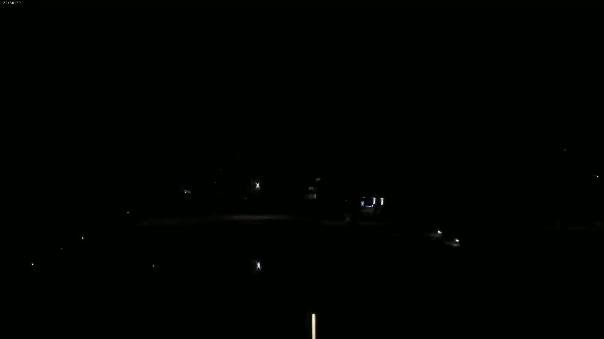A dark, nighttime scene shows a few faint lights from buildings and vehicles in the distance.