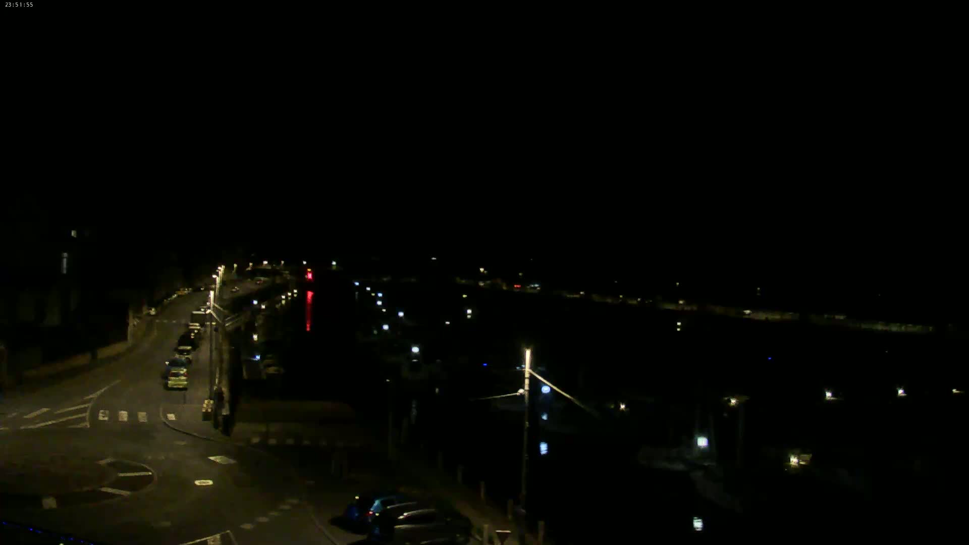 A nighttime, high-angle view of a dark road intersecting with a body of water lined with faintly lit docks.