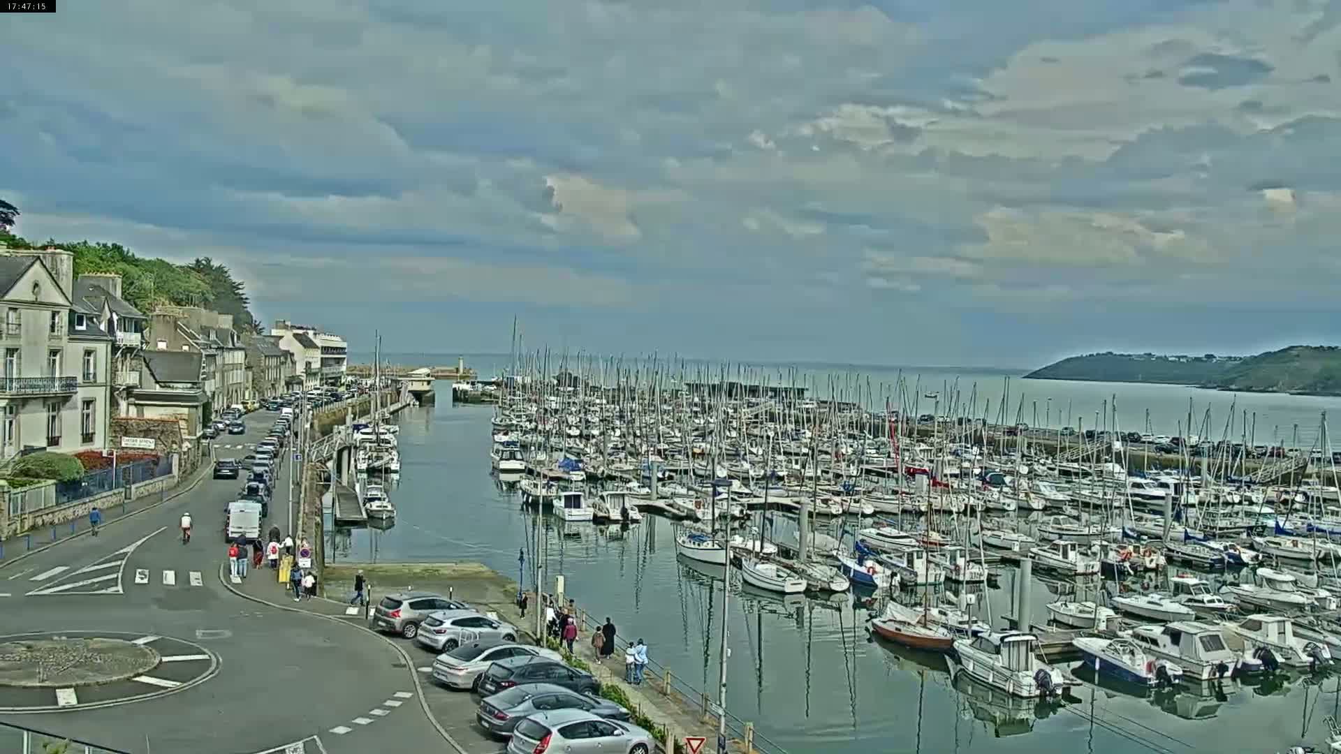 A coastal town with a marina filled with numerous sailboats and motorboats under a partly cloudy sky.