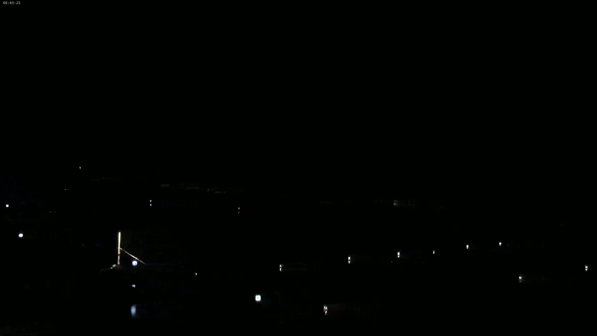 A nighttime view shows a dark body of water with sparsely scattered lights along the shore and in the distance.