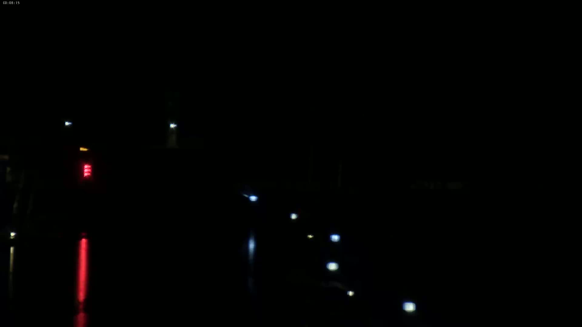 At night, the taillights of a vehicle and the headlights of several other distant vehicles are visible on a dark, wet road.