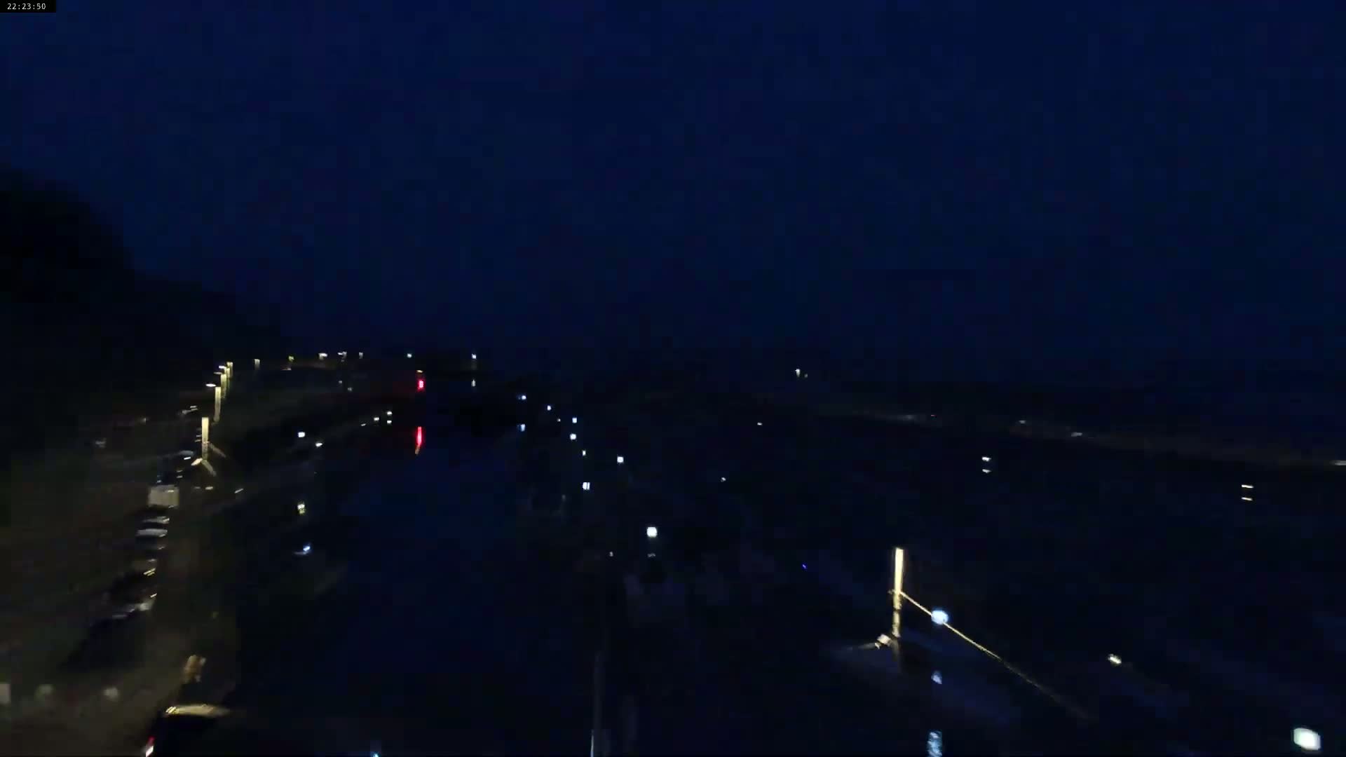 A dark nighttime scene shows a waterway with dimly lit roads and parked cars on either side under a clear, dark sky.