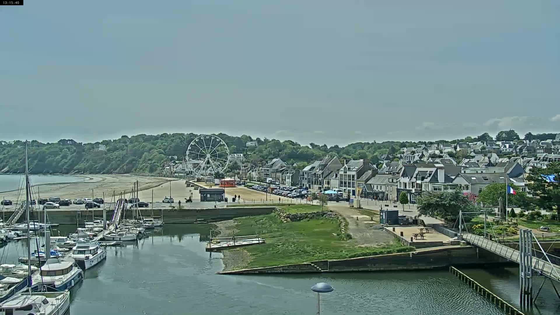 A coastal town with a marina full of boats, a sandy beach, a Ferris wheel, and numerous buildings under a mostly clear sky.