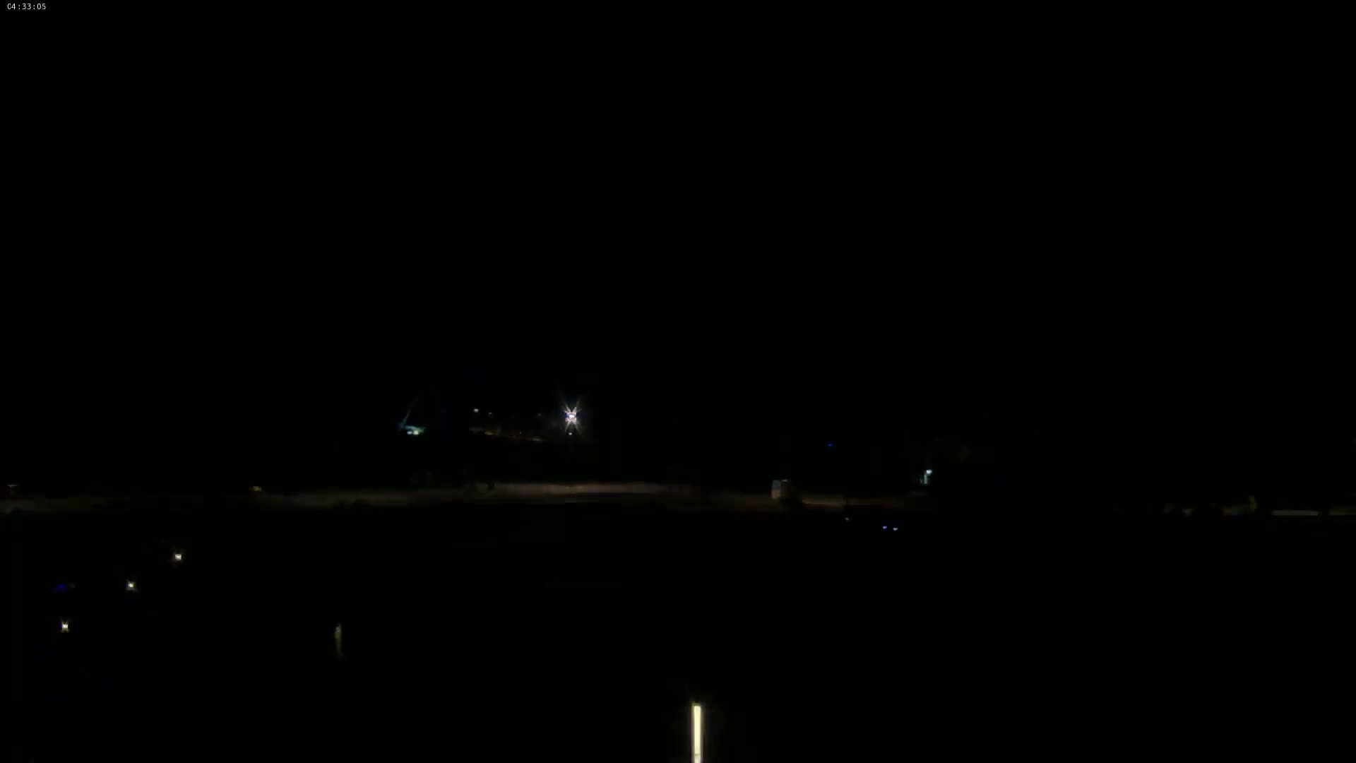 A dark, nighttime scene shows a flat, empty expanse of land with a few faint lights visible in the distance.