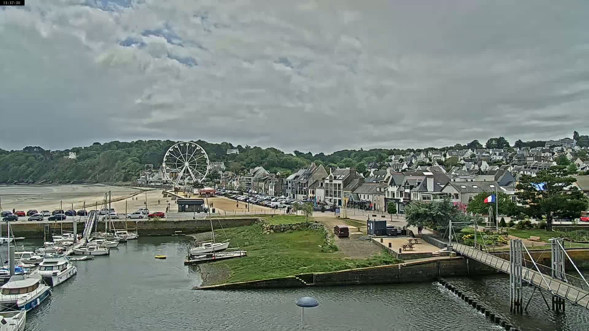A coastal town with a Ferris wheel, a marina filled with boats, and a sandy beach under a cloudy sky.