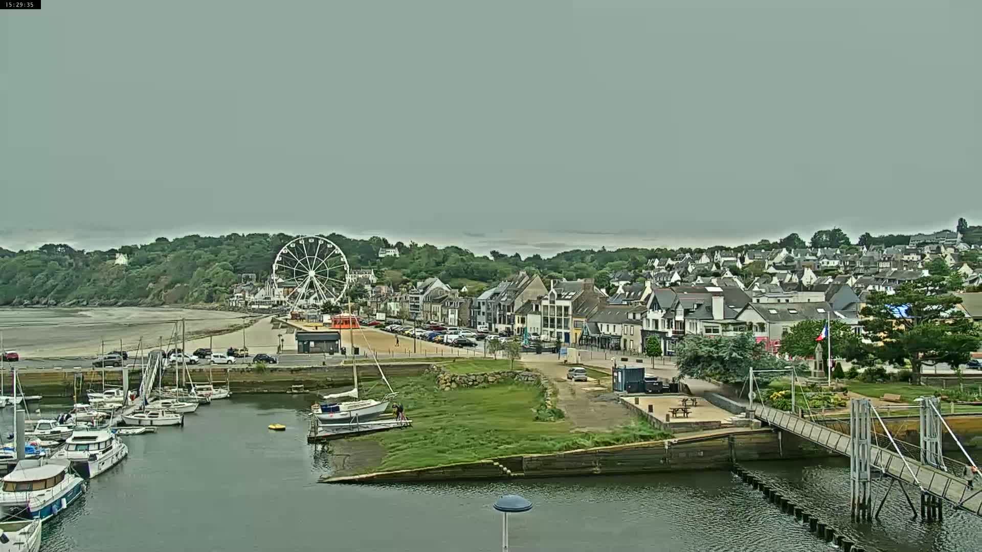 A harbor filled with boats sits before a town with a Ferris wheel under an overcast sky.