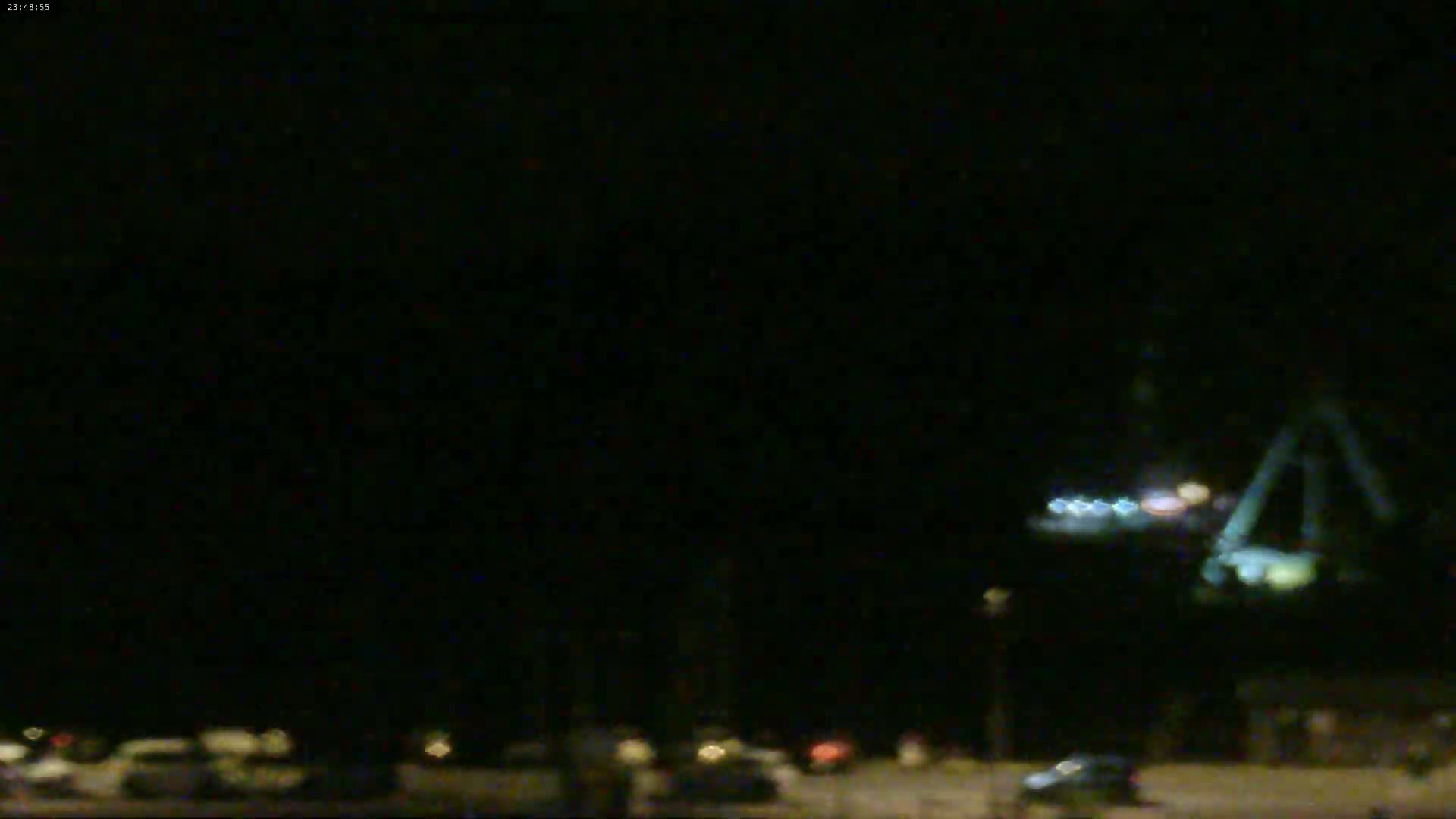 A dimly lit parking lot at night, with a blurry structure and lights visible in the distance.