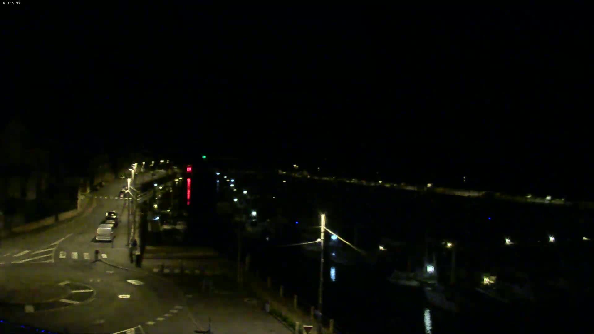 A nighttime view of a harbor with boats and a road with cars, under a dark sky.