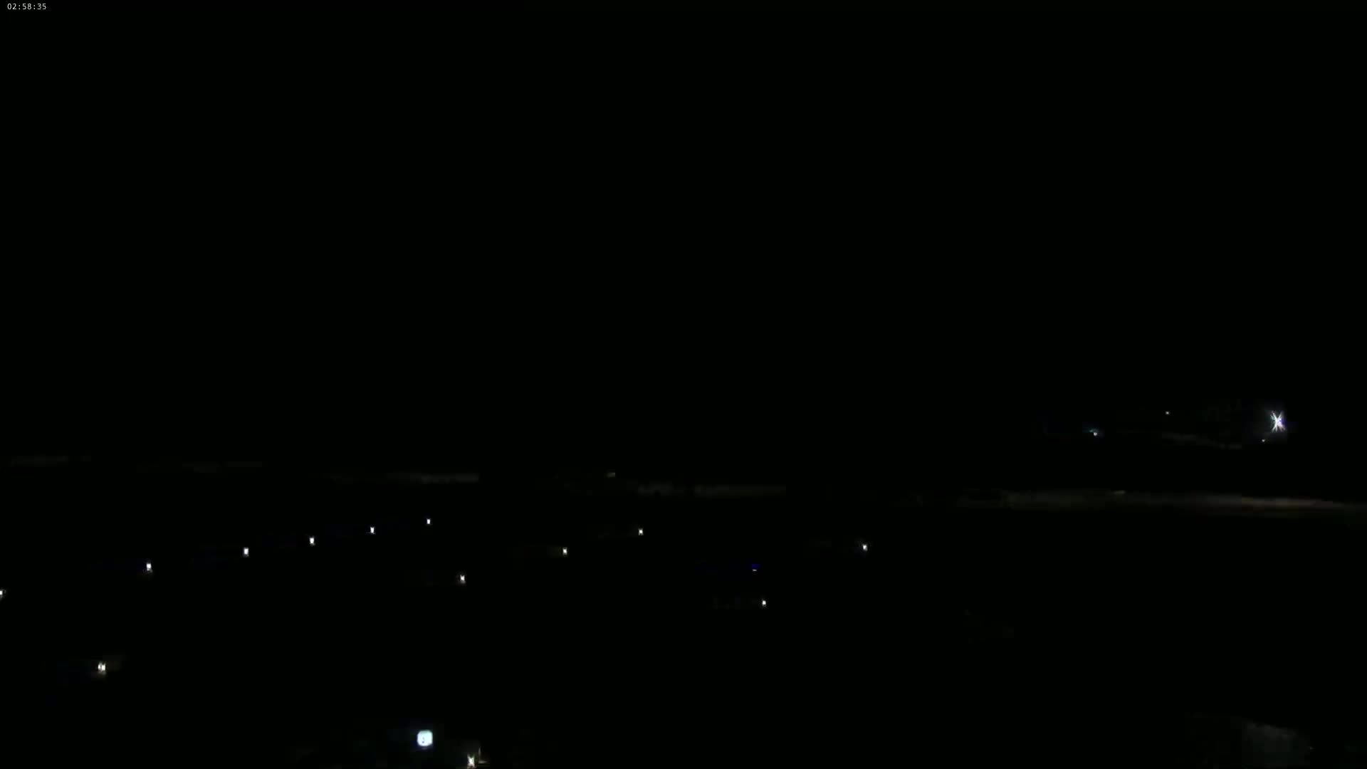 A dark, nighttime scene shows a few scattered lights on the ground under a completely black sky.