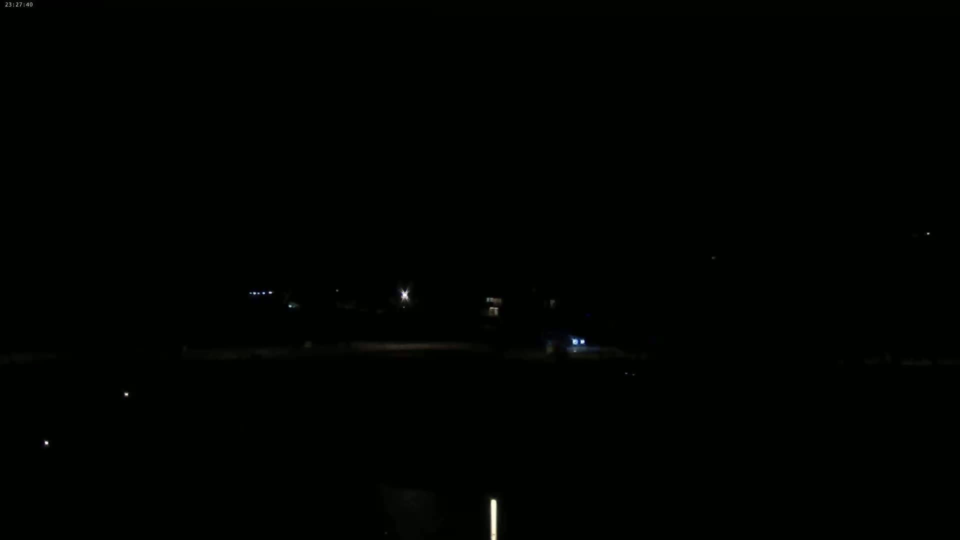 A dark, nighttime scene shows dimly lit buildings and a few scattered lights in the distance.