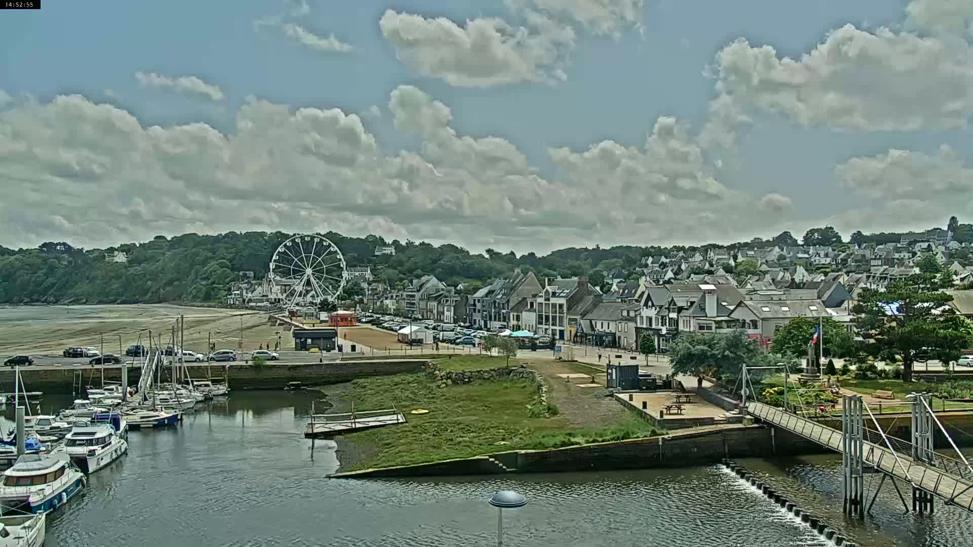 A coastal town with a Ferris wheel on the beach, a marina full of boats, and a bridge under partly cloudy skies.