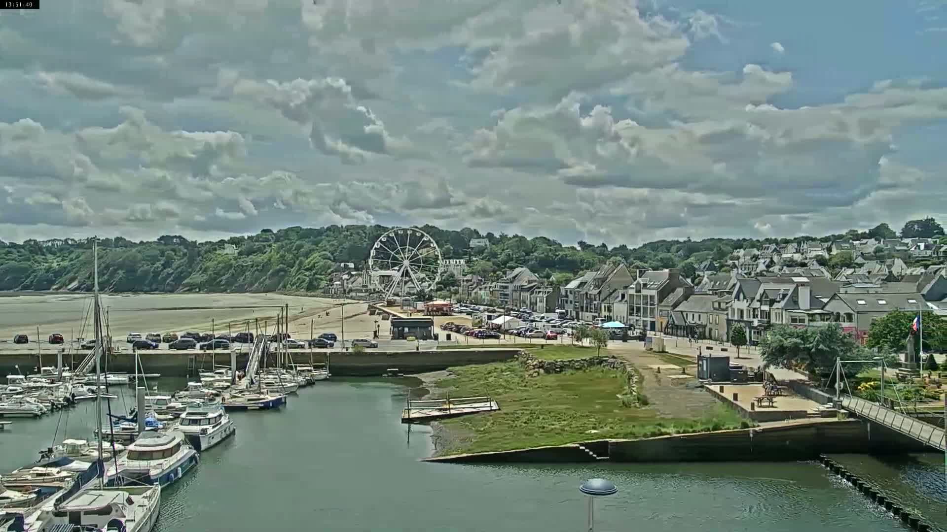 A harbor filled with boats is situated near a town with a Ferris wheel under a partly cloudy sky.