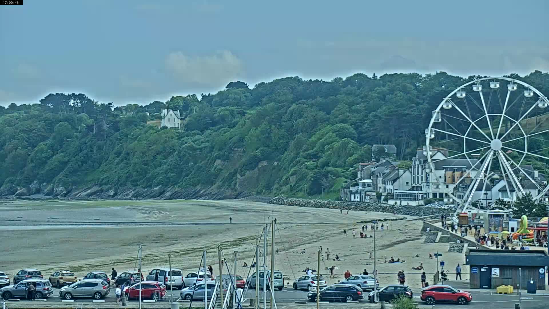 A sandy beach with a Ferris wheel, several buildings, and parked cars is visible under a partly cloudy sky.