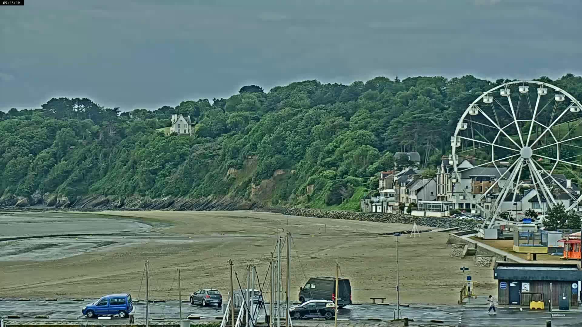 A Ferris wheel sits on a beach near a seaside town under an overcast sky.