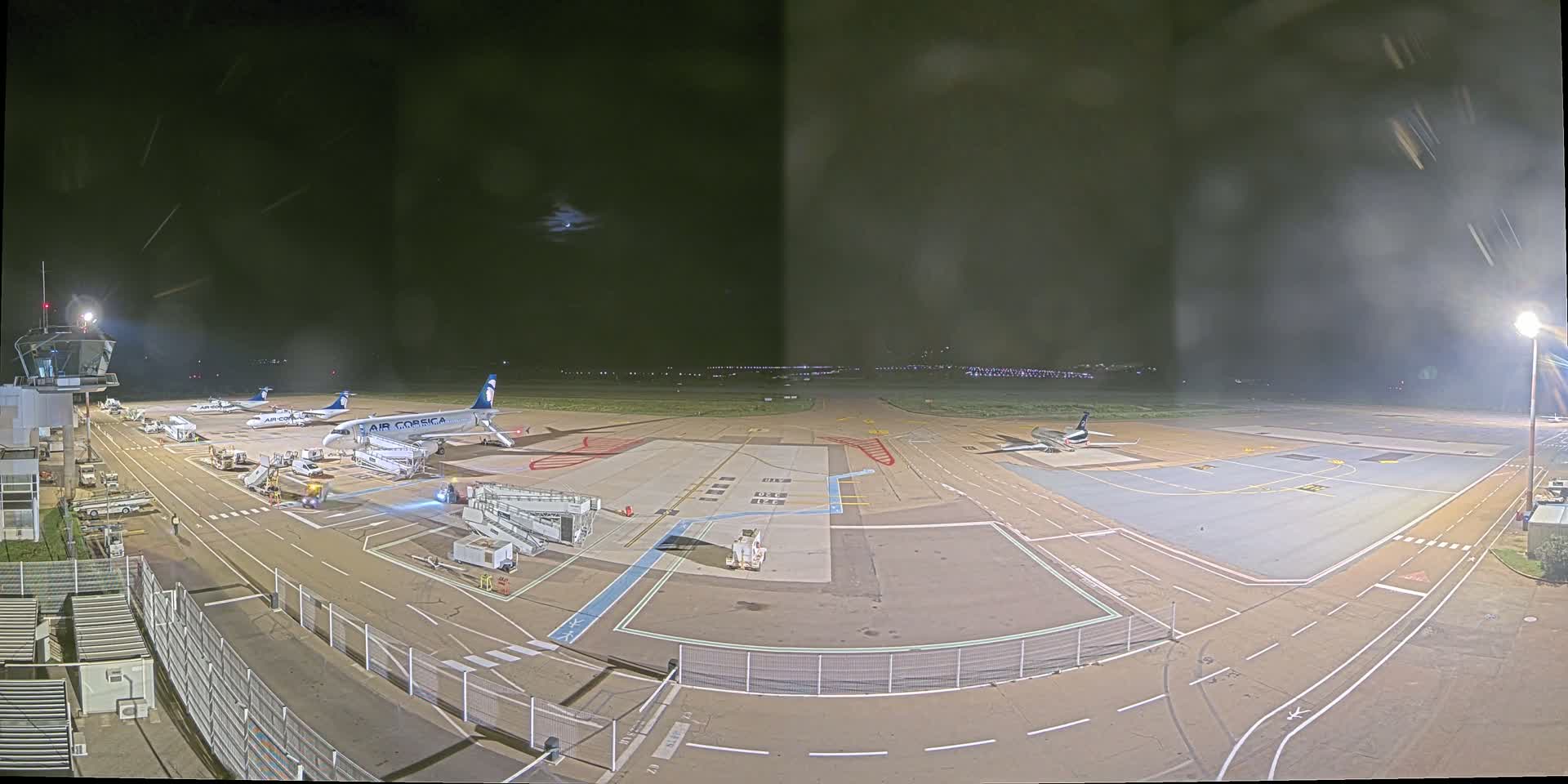 A nighttime view of an airport tarmac with several airplanes parked near gates and service vehicles, under a dark, cloudy sky.