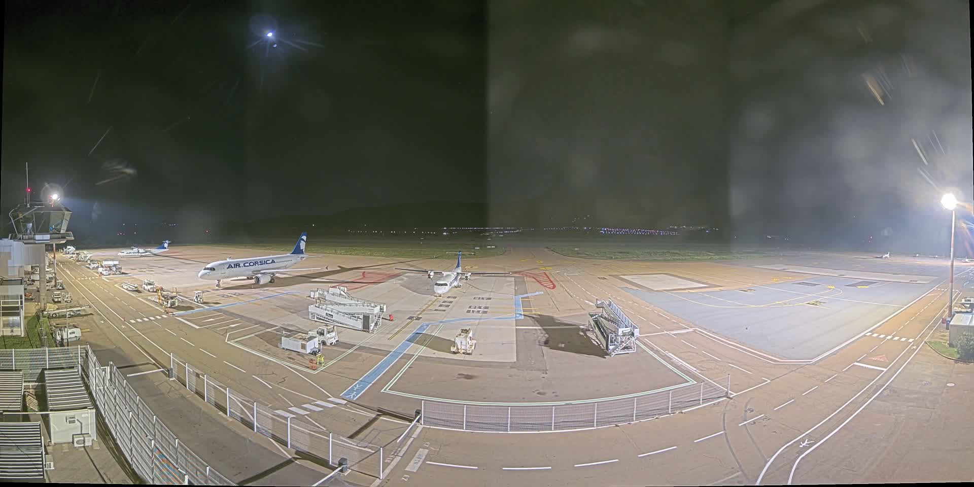 A nighttime view of an airport tarmac with several airplanes, ground support equipment, and airport infrastructure under a clear, moonlit sky.