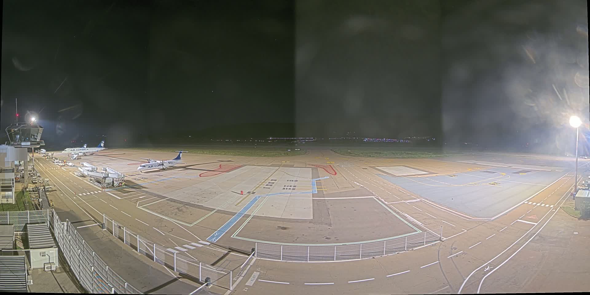 A nighttime view of an airport tarmac with two airplanes parked near a terminal building under a dark, cloudy sky.
