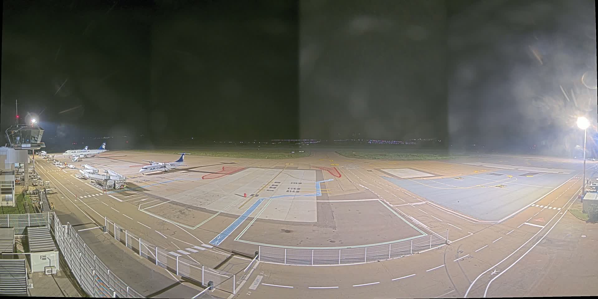 A nighttime view of an airport tarmac with two airplanes parked near a terminal building under hazy conditions.