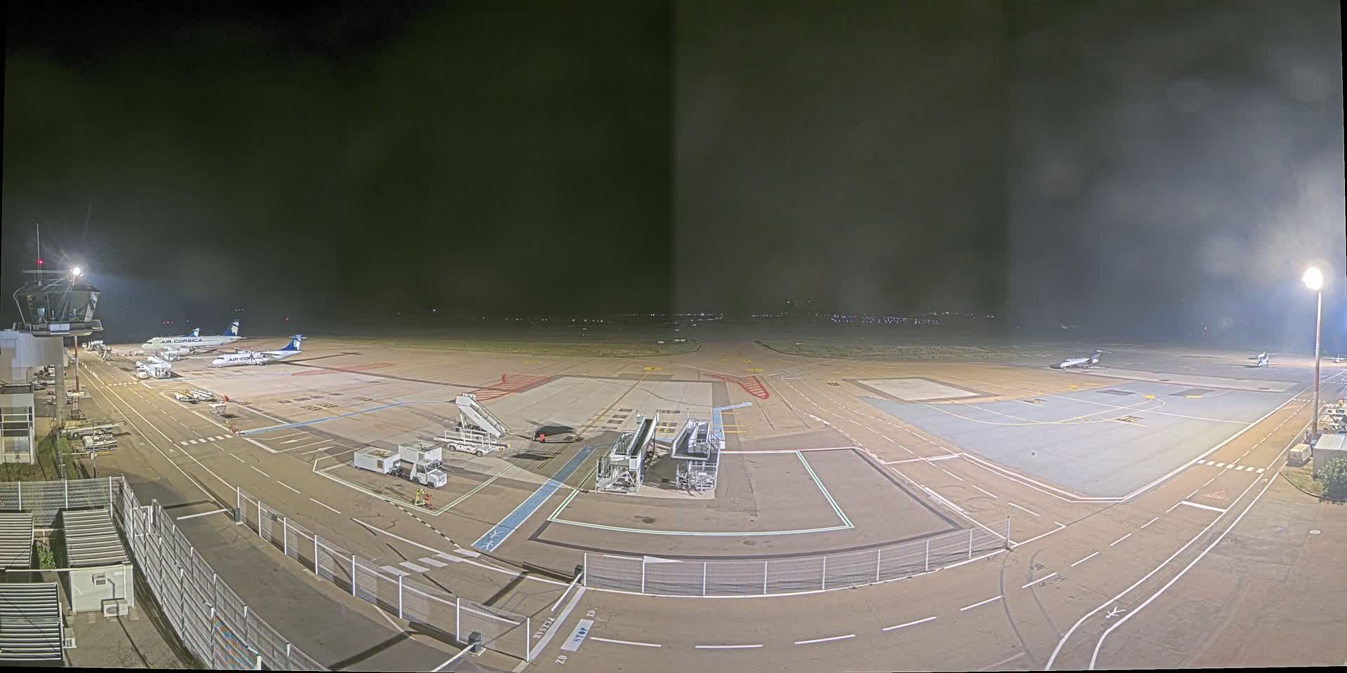 A nighttime view of an airport tarmac with several airplanes parked near gates and jet bridges, under hazy conditions.