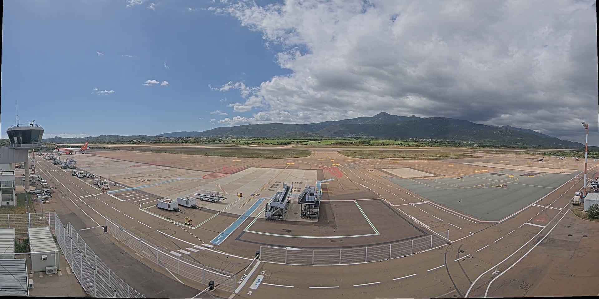 An airport tarmac under a partly cloudy sky with mountains in the distance.