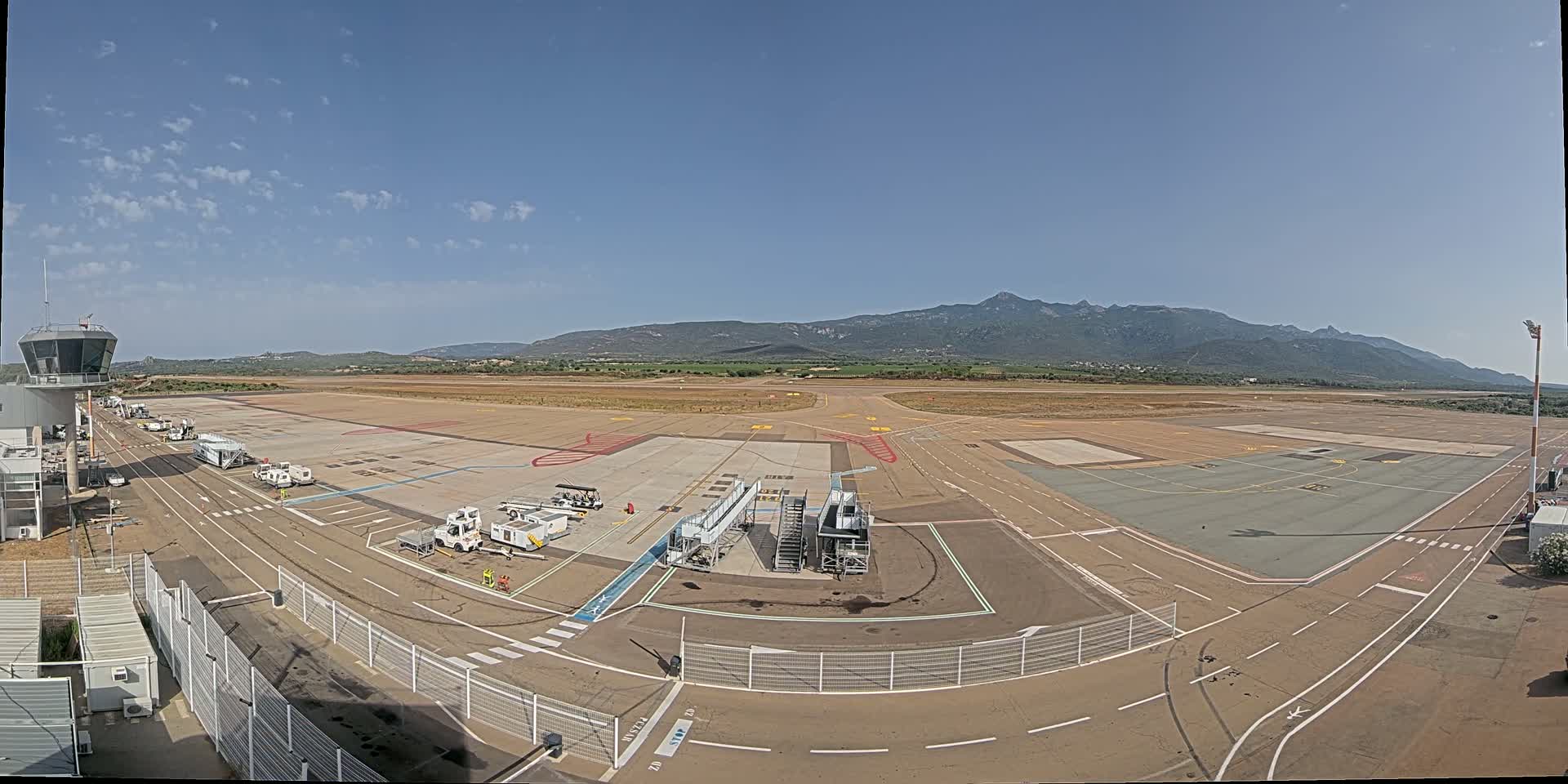 A mostly empty airport tarmac under a clear sky, with mountains visible in the distance.