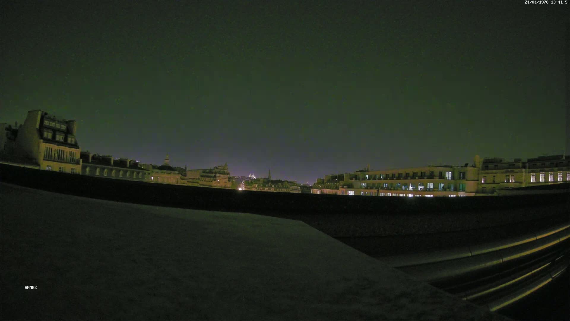 A nighttime cityscape is seen from a rooftop, under a dark, clear sky.