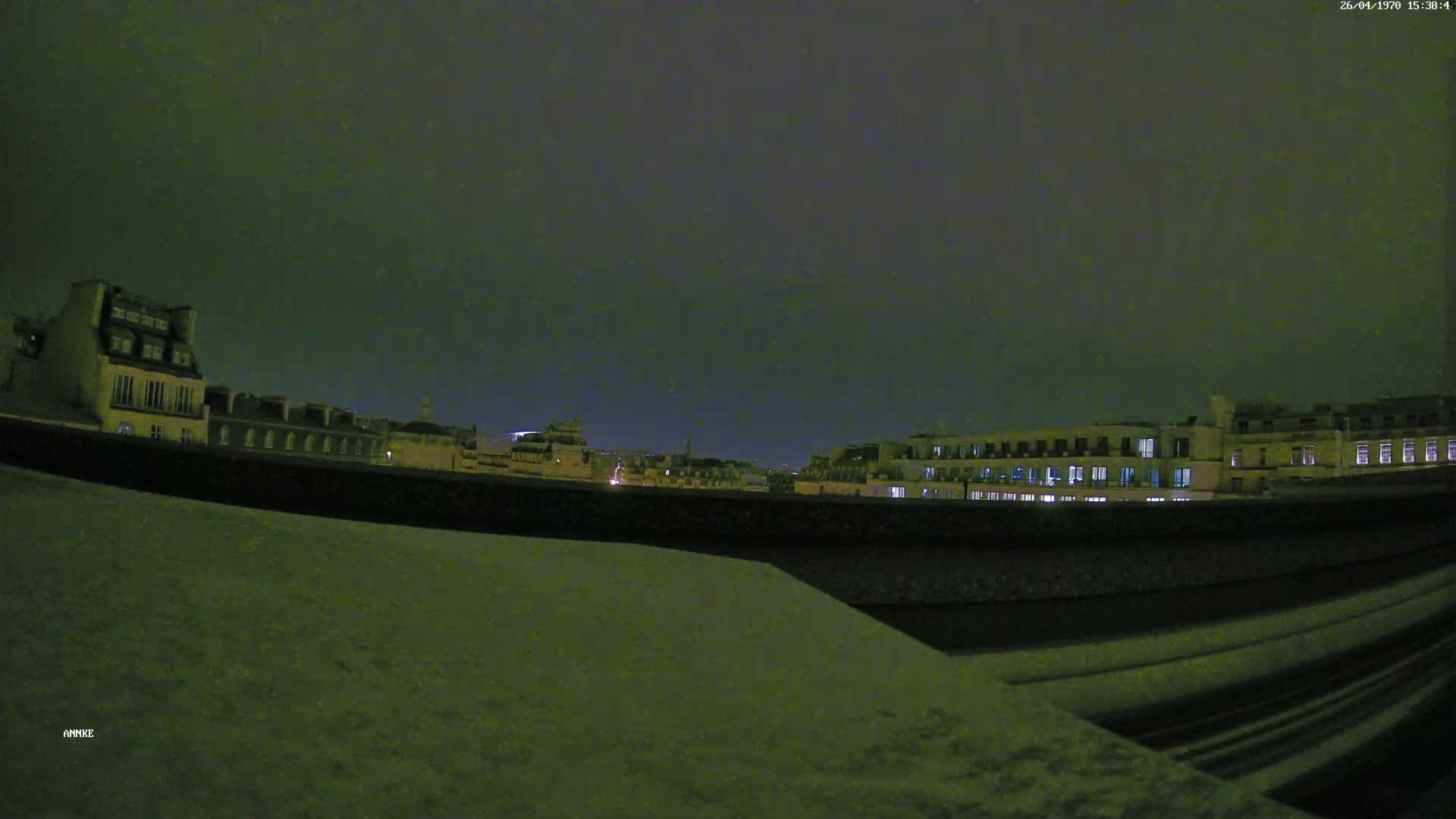 A nighttime view of city buildings from a snow-covered rooftop under a dark, cloudy sky.