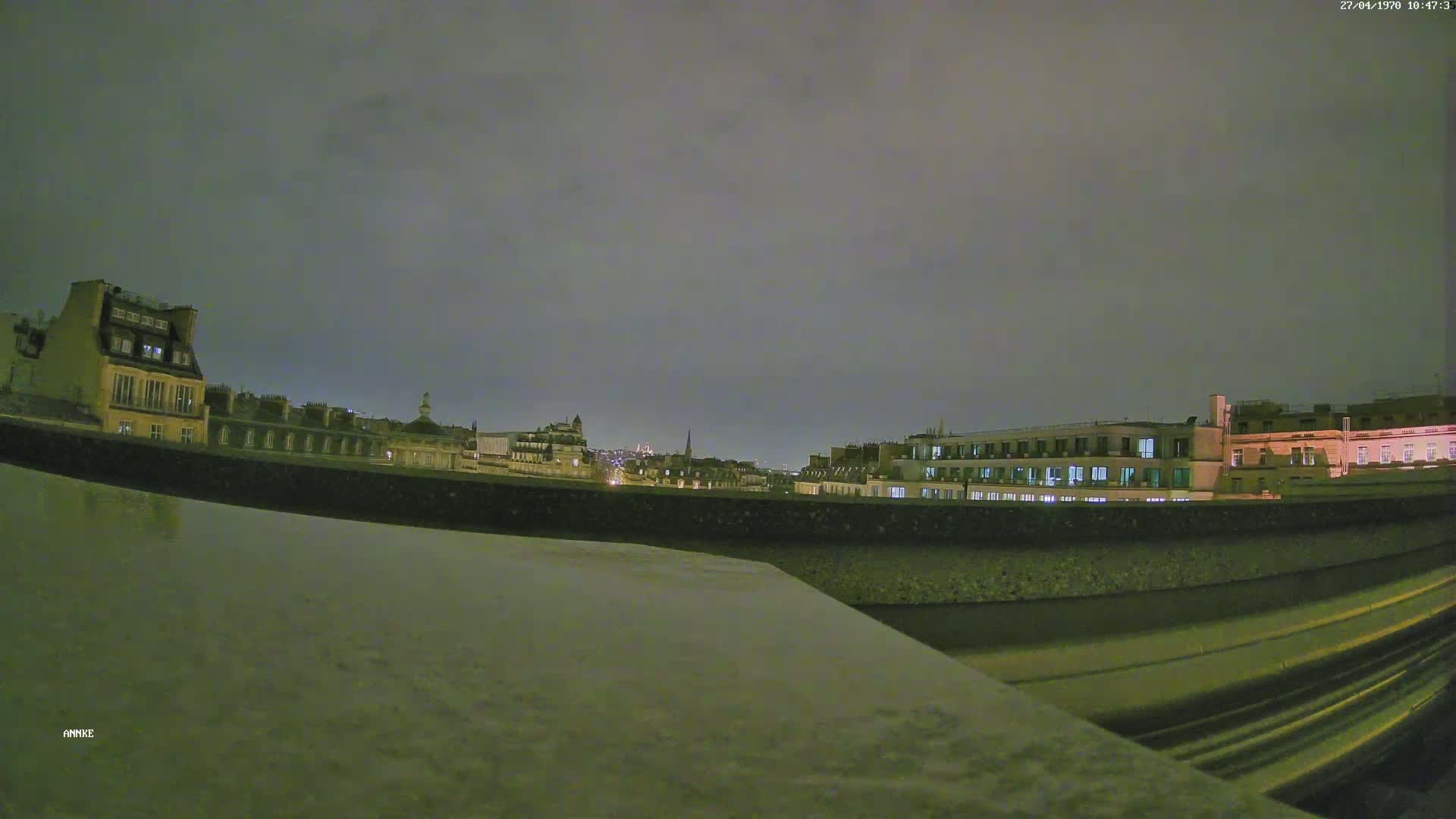 A nighttime view of city buildings and a roadway under a cloudy sky.