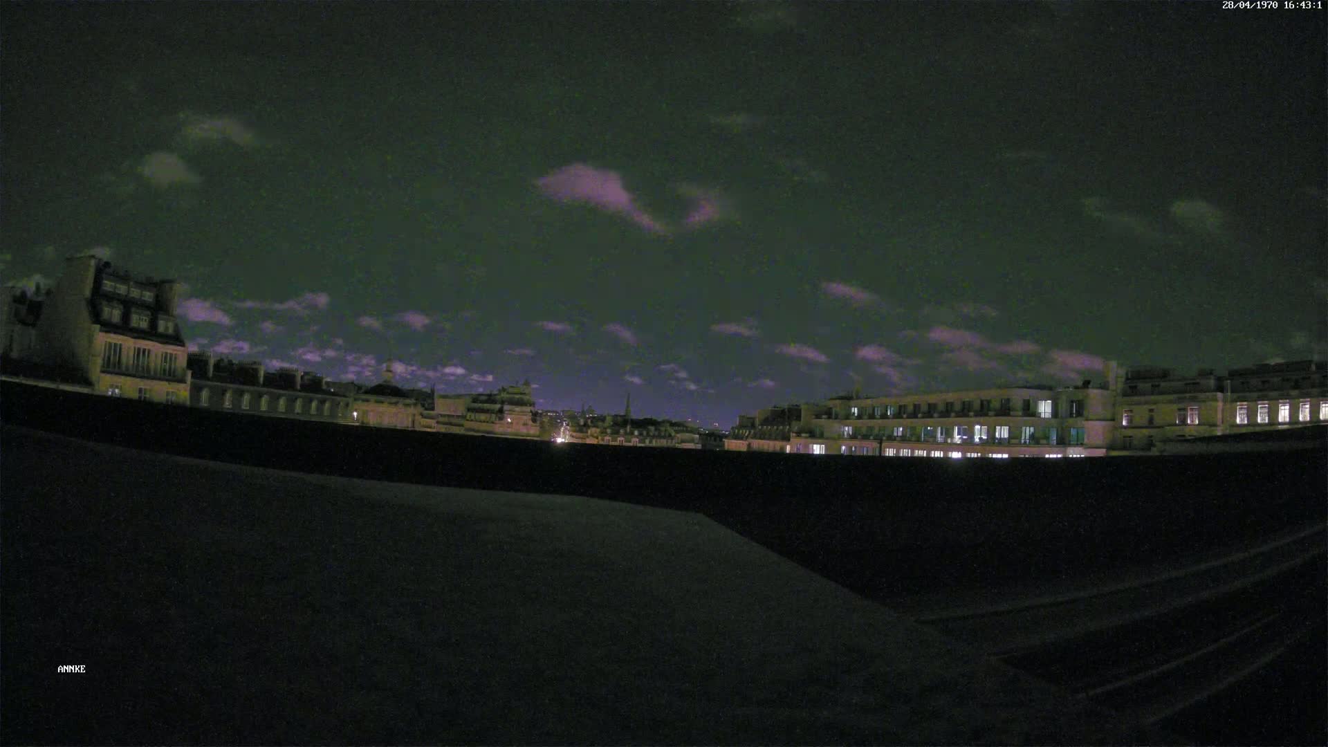 A nighttime cityscape of buildings with some lights visible under a partly cloudy sky.