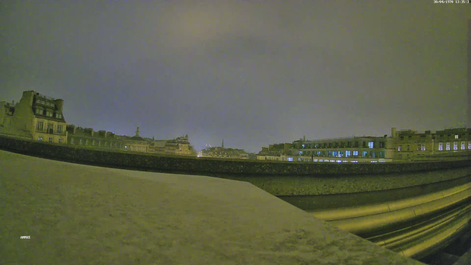 A nighttime view of city buildings from behind a low wall under an overcast sky.
