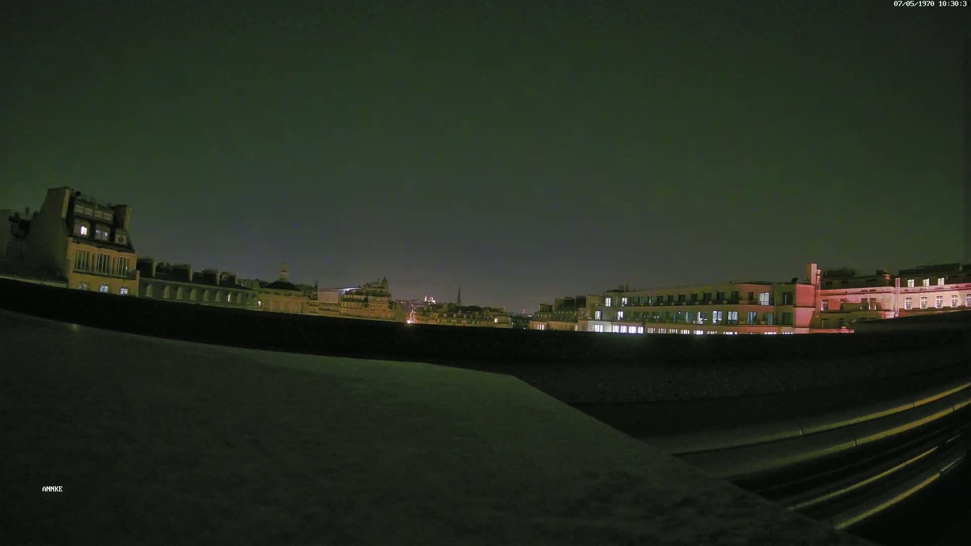 A nighttime cityscape view of several buildings with some lights on, under a dark, clear sky.