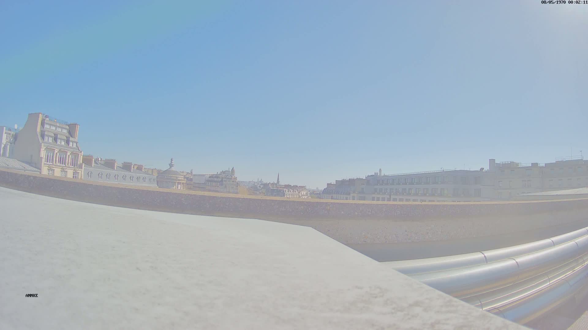 A rooftop view of city buildings on a clear, sunny day, with large metal pipes visible in the foreground.