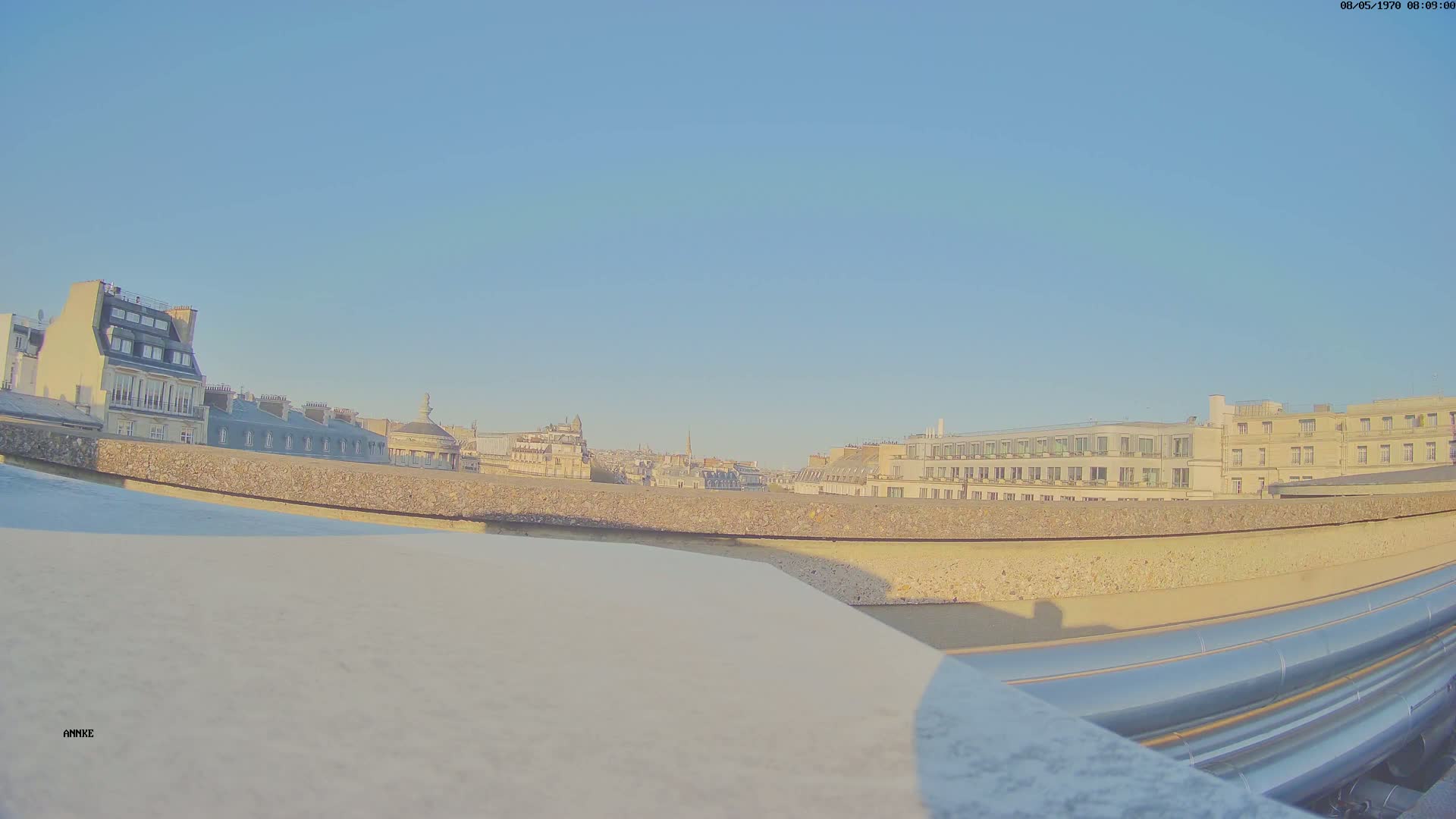 A rooftop view of a city under a clear blue sky shows a row of buildings stretching into the distance.