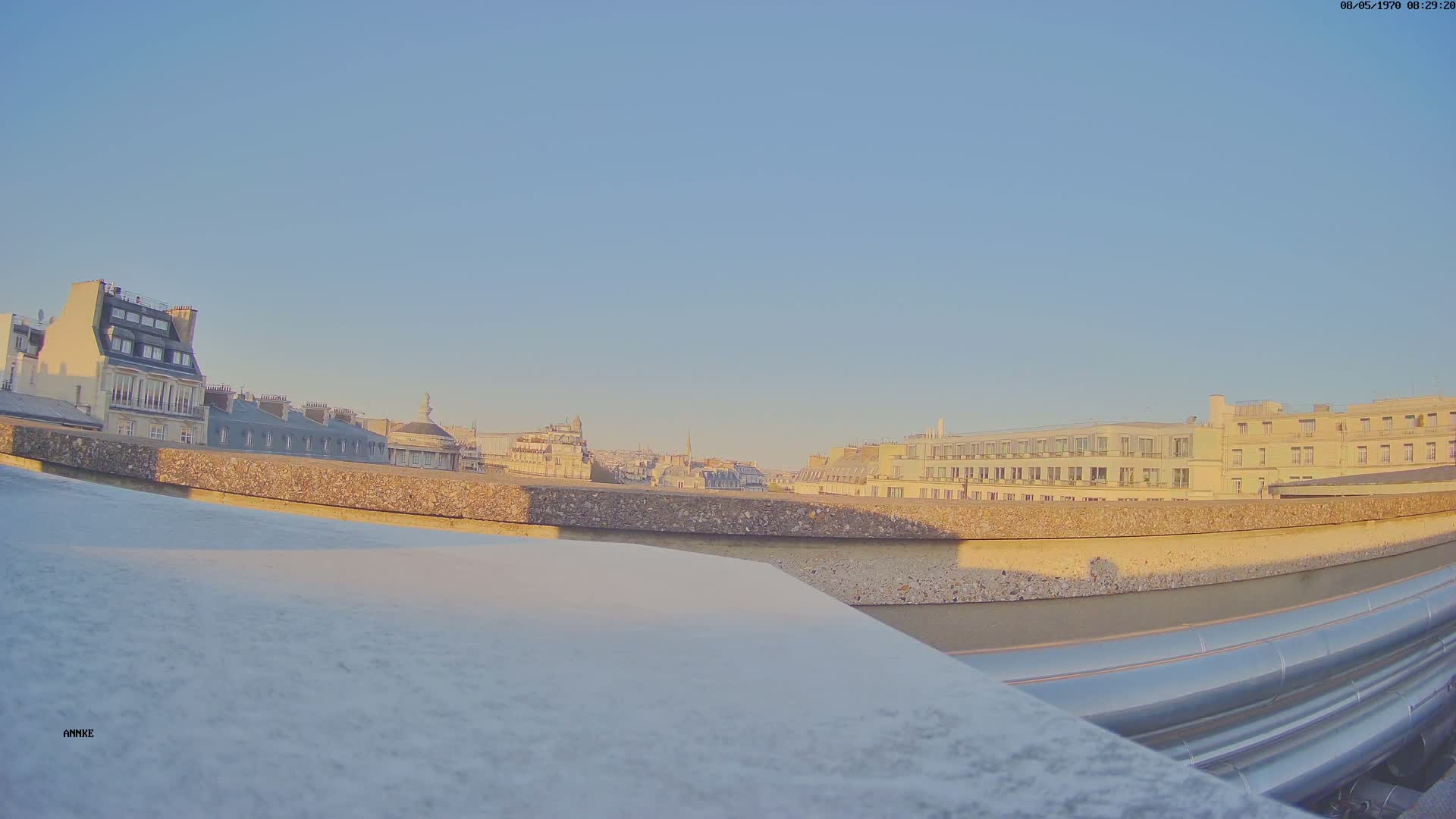 A rooftop view of Parisian buildings under a clear, pale-blue sky.