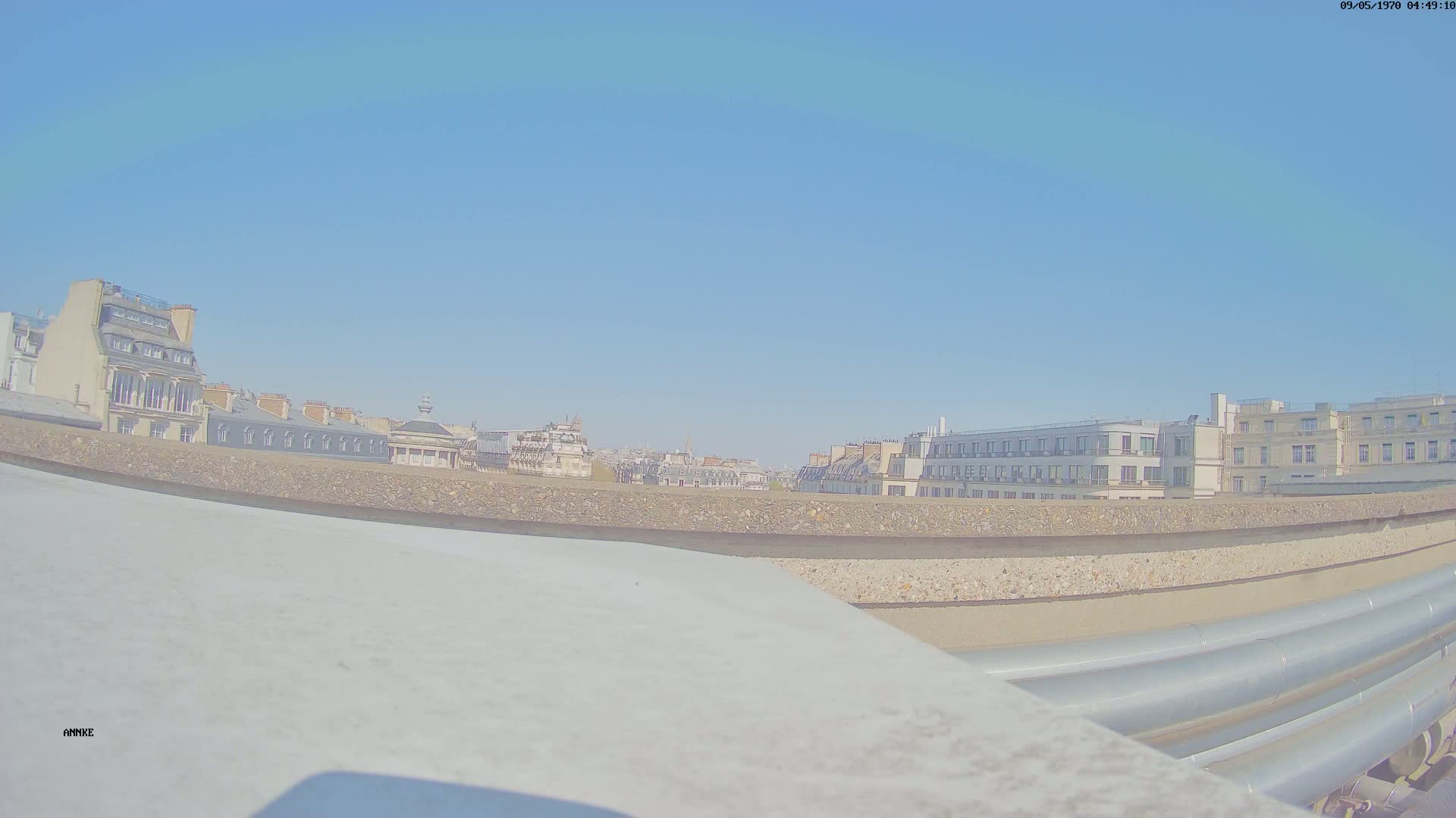 A city skyline of multi-story buildings is visible under a clear blue sky from a rooftop vantage point.