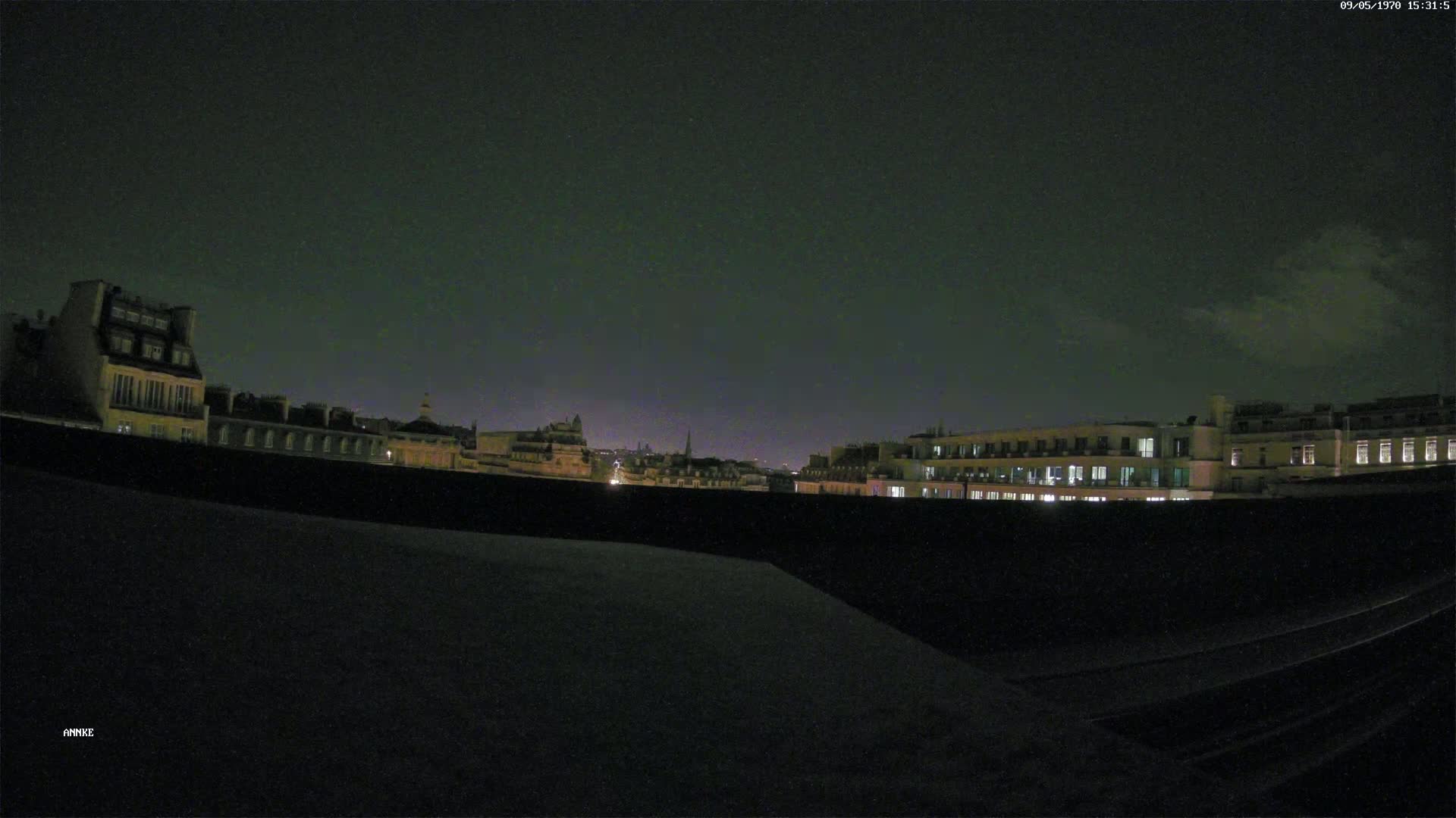 A nighttime cityscape of buildings with some lights visible under a mostly dark sky with a few clouds.