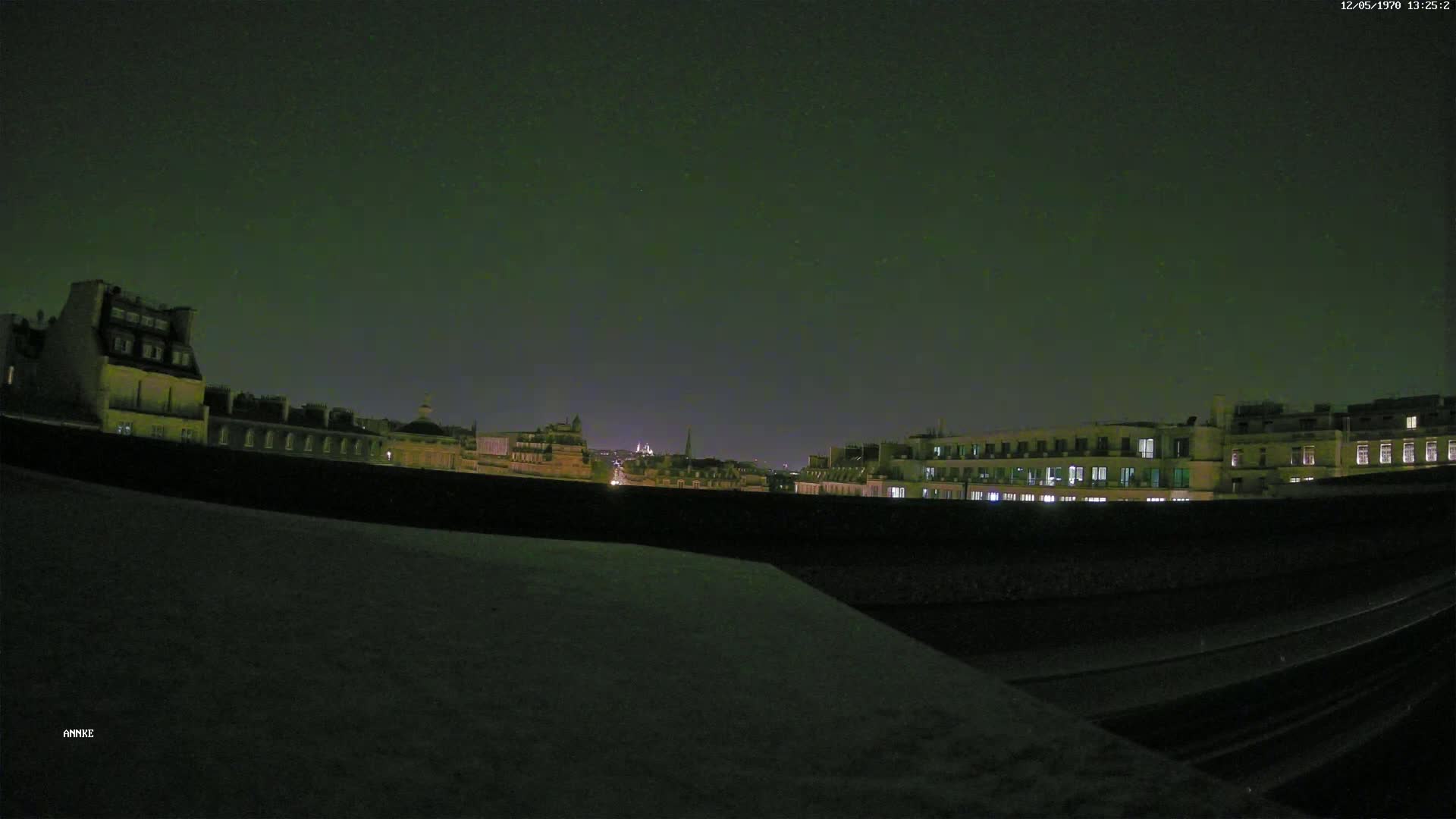 A nighttime view of a city skyline with dark buildings and some lights visible under a dark, clear sky.