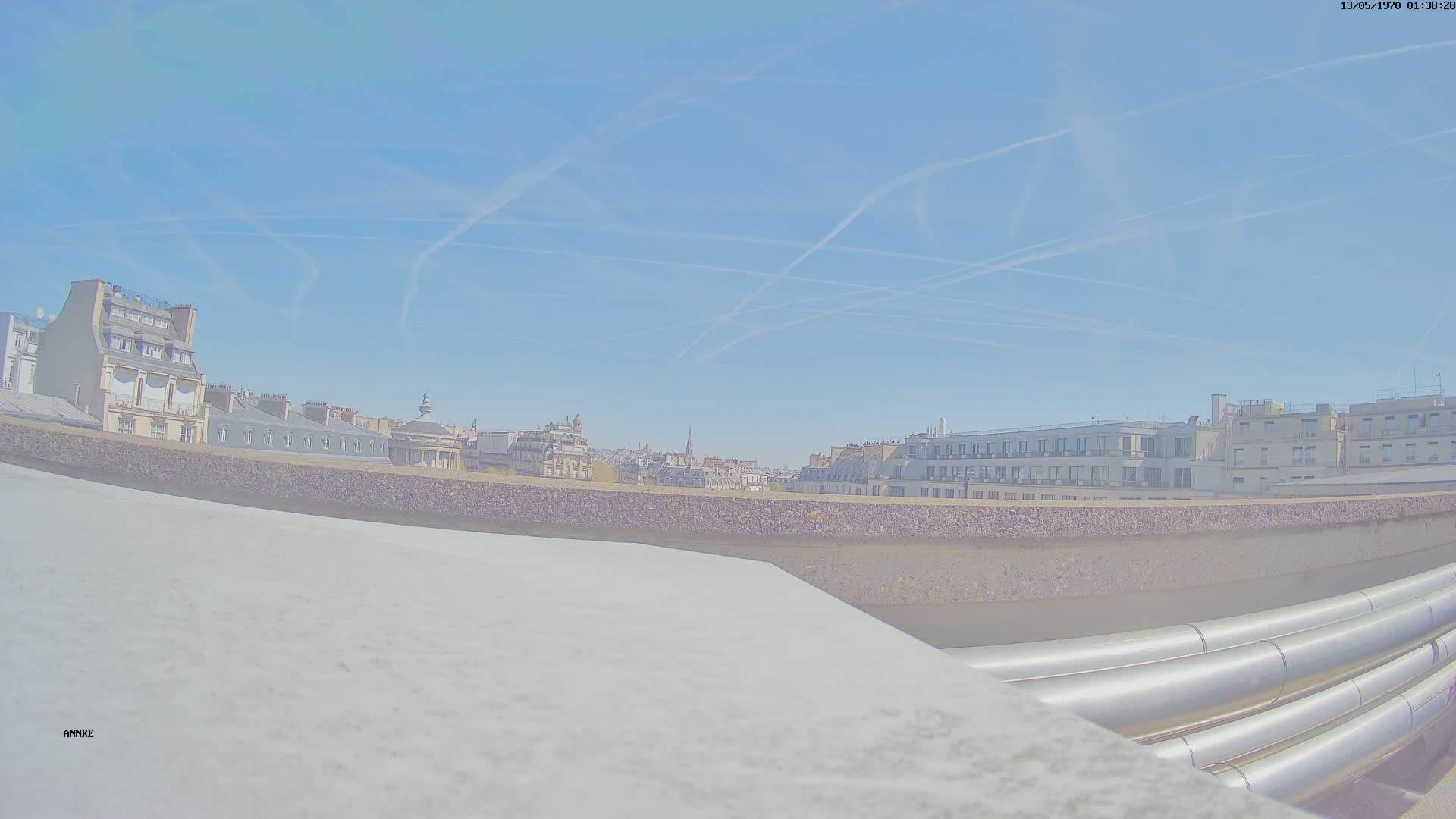 A city skyline with multiple buildings under a clear blue sky with contrails.