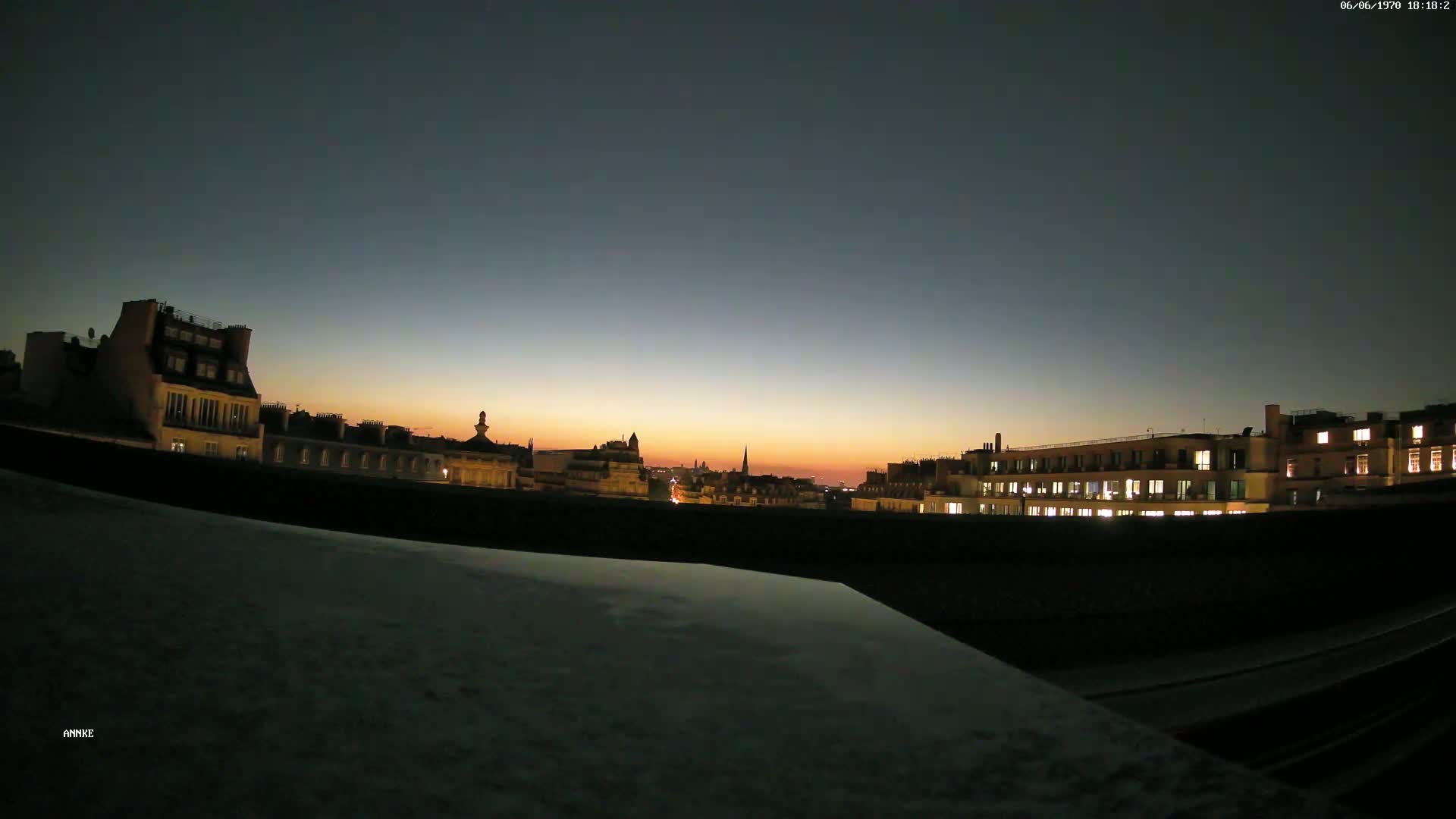A city skyline at sunset, with some buildings lit up, is viewed from a rooftop.
